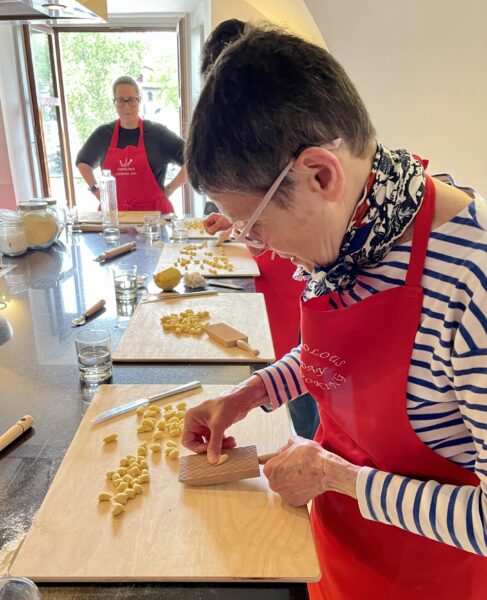 Woman shaping cavatelli pasta on a wooden board.
