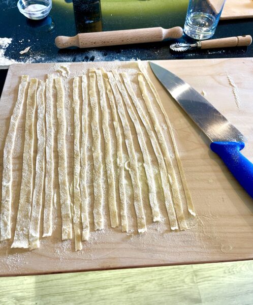 Freshly cut strips of tagliatelle with a knife on a board.