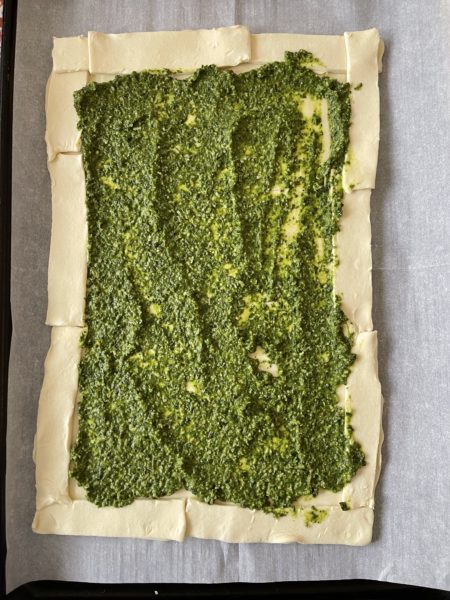 Puff pastry crust spread with pesto.