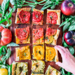 Cut pieces of heirloom tomato tart and a hand reaching for a piece.