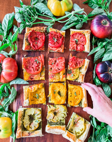 Cut pieces of heirloom tomato tart and a hand reaching for a piece.
