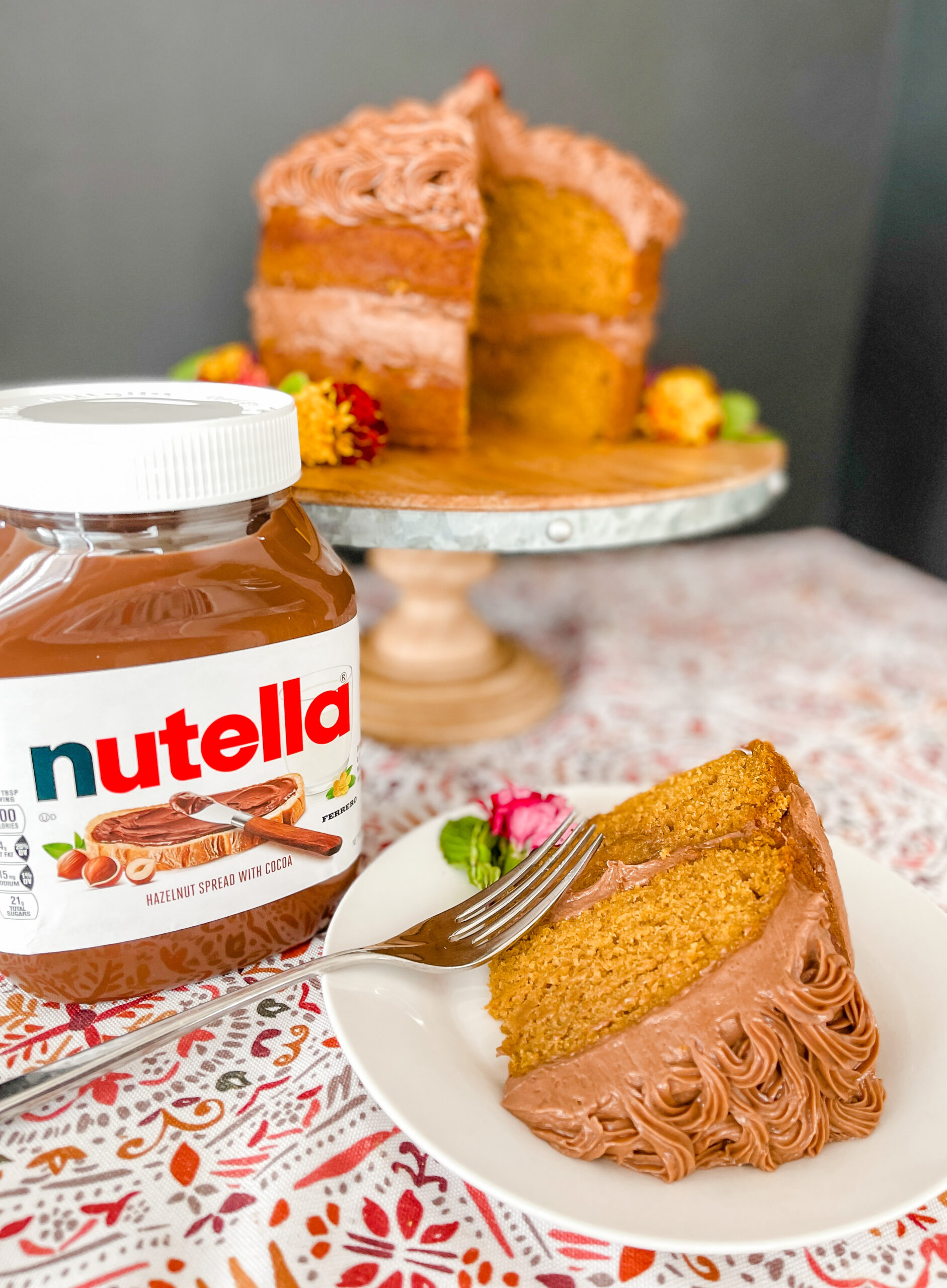 Cake slice with Nutella jar and full cake in the background.