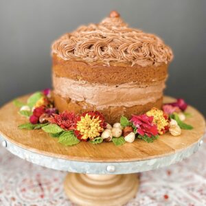 Nutella Pumpkin Cake on a stand with hazelnuts and flowers.