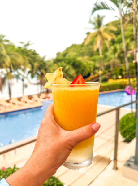 Hand holding tropical cocktail in front of pool.