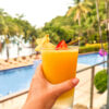 Hand holding tropical cocktail in front of pool.