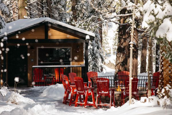 Cabins in the snow around a campfire and red chairs.