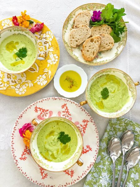 Bowls of avocado soup in china with slices of bread on a plate.