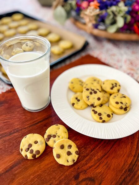 Mini chocolate chip cookies on a plate with a glass of milk.