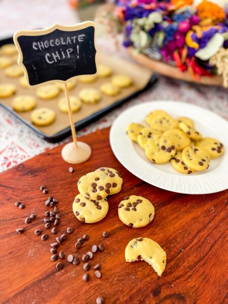 Mini chocolate chip cookies with scattered chips and a hand-written Chocolate Chip sign. 