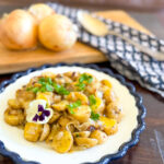 Potato salad on a plate with onions on board behind it.