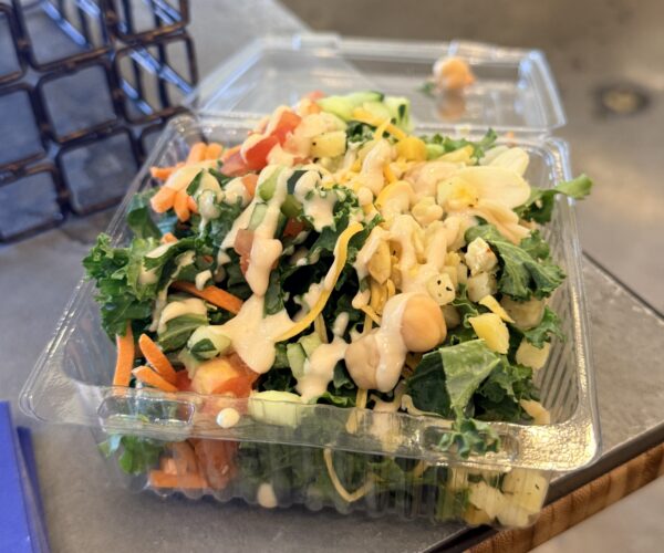 Plastic container with kale salad and lemon tahini dressing.