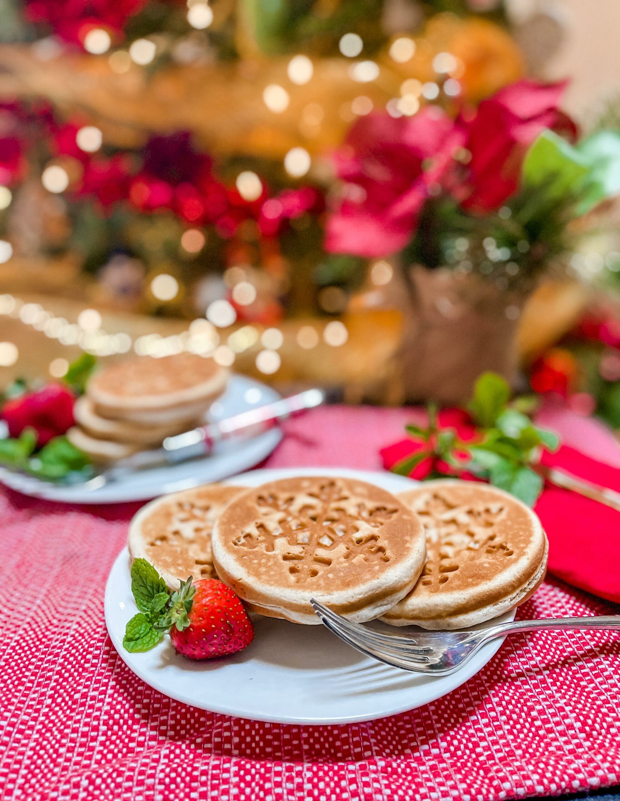 Three gingerbread waffles on a plate in front of Christmas tree.