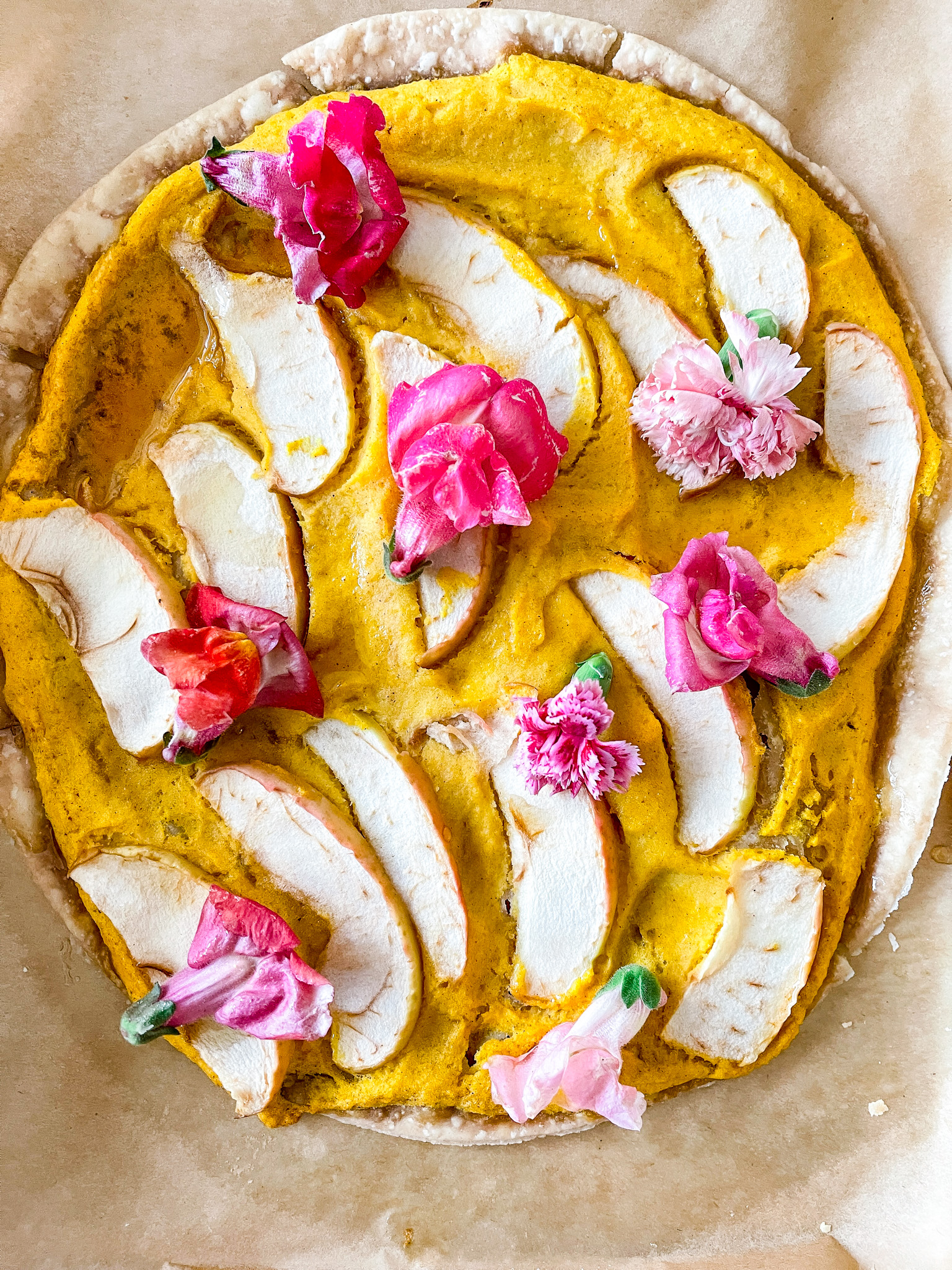Overhead view of sweet butternut squash flatbread with apples and edible flowers.
