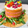 White cake with layers of rhubarb curd topped with mint leaves, edible flowers, and raspberries.