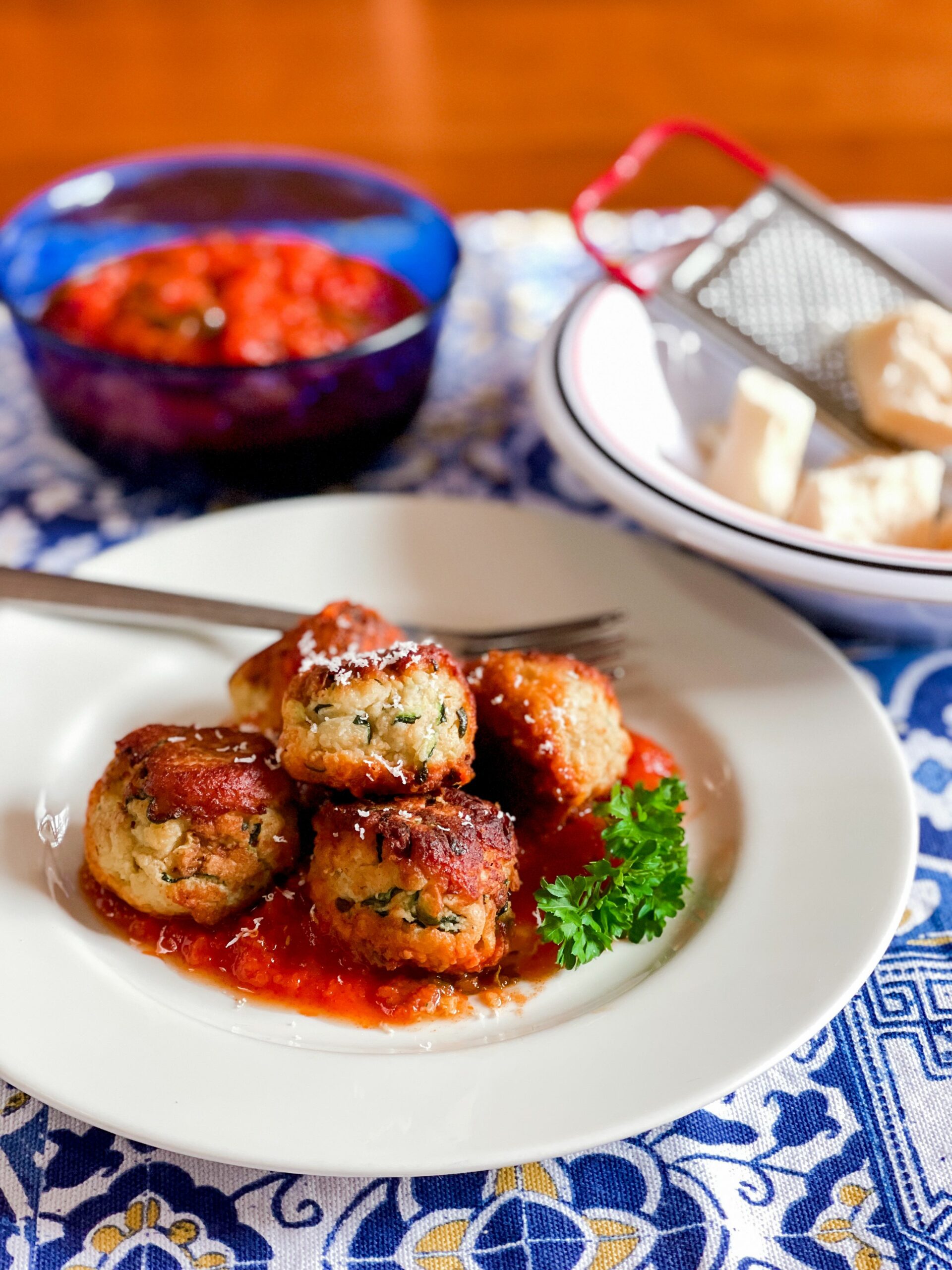 zucchini meatballs on plate with tomato sauce and cheese on table.
